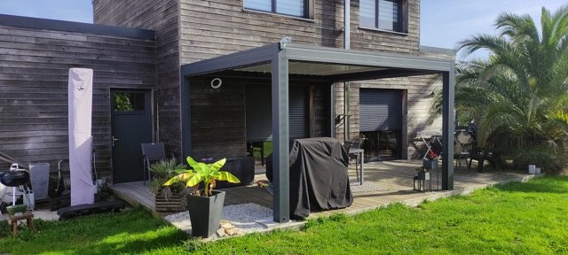 Pergola bioclimatique anthracite adossée à une maison en bardage bois, posée à Plougoumelen