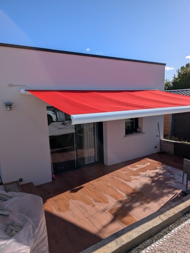 Store banne coffre blanc à toile rouge déployé au-dessus d'une terrasse
